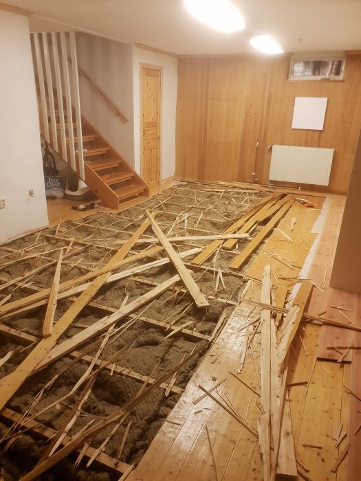 Källargolv under renovering med upprivna träreglar och isolering synlig på betongplattan.