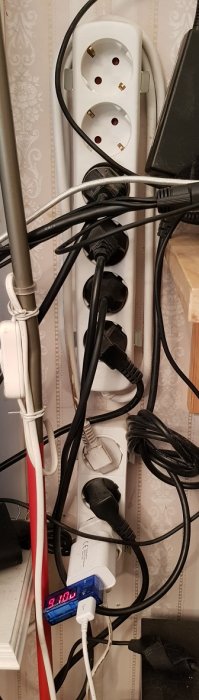 En överbelastad grenkontakt med flera anslutna sladdar och kablar som hänger löst, vid en arbetsplats.