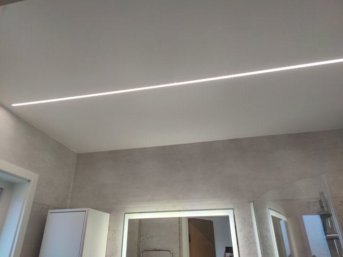 LED-list infälld i taket ger en skarp ljuslinje över en modernt inredd rumsmiljö.