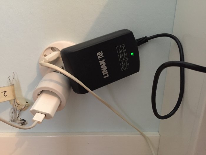 Stor nätdel i vägguttag i spänd position mot andra pluggar, gammal telefonkabel syns.
