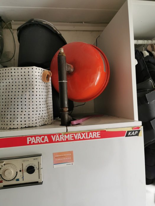Gammal Parca värmeväxlare och ett rött Zilmet 12 L expansionskärl ovanpå i ett förrådsutrymme.