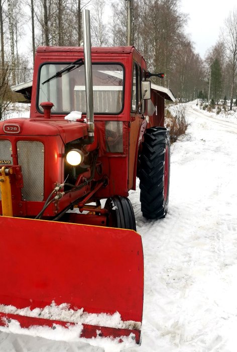 Röd traktor med modifierad tunn ljuddämpare på sidan i ett snöigt landskap.