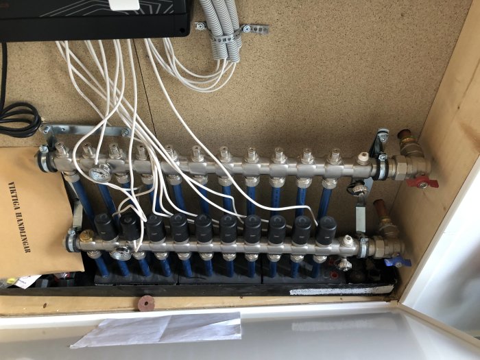 Golvvärmefördelare med flera kopplade termostater och rörarrangemang i en teknisk skåpinstallation.