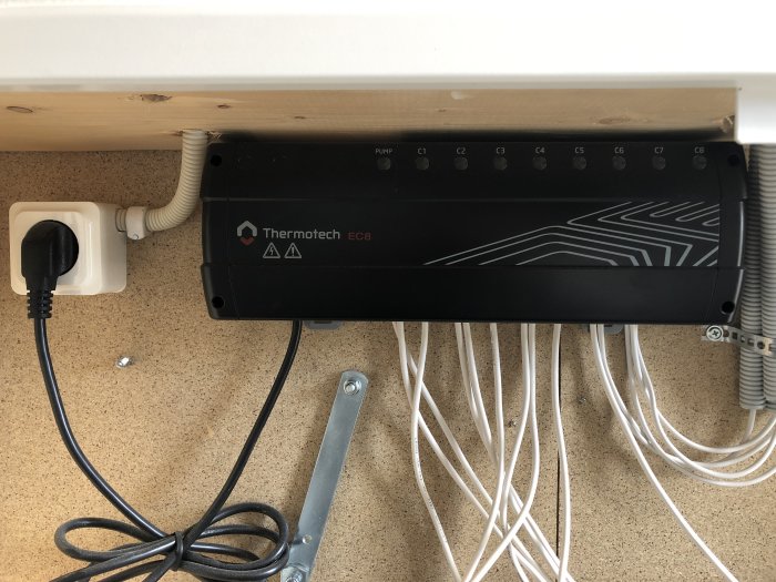 En svart styrutrustning märkt "Thermotech EC8" och dess kablar monterade på en vägg, utan synlig belysning.