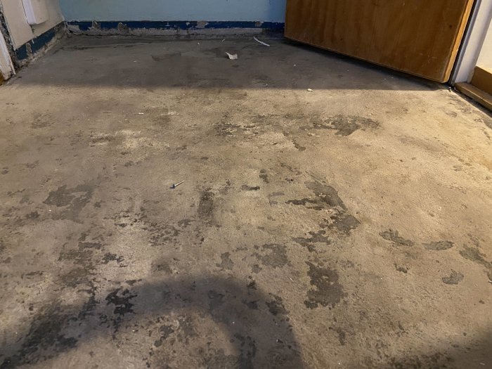 Gammalt betonggolv i en lägenhet med rester av svartlim före renovering och läggning av ny klinker.