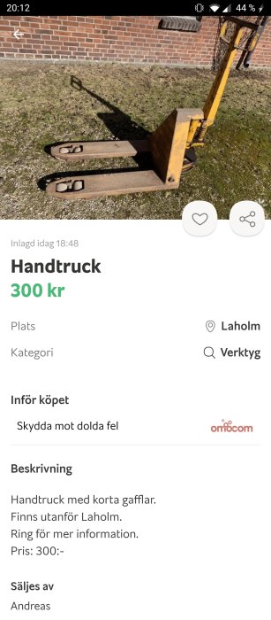 Gul handtruck står framför en tegelvägg på en gräsbevuxen mark.