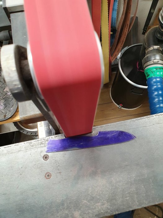 Blad fastsatt nära slipmaskins röda slipband på verkstadsbänk, redo för finslipning.