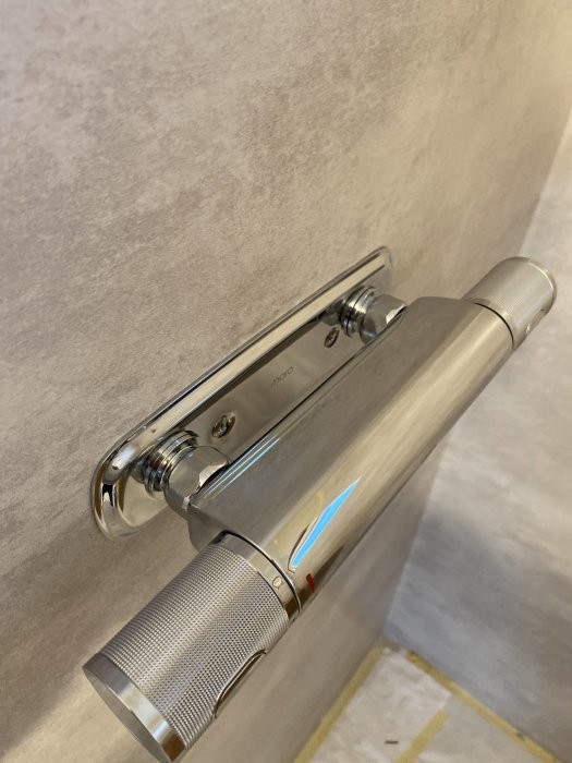 Blandarfäste i badrum med nära väggkapade rör och synliga skyddsrör mot plastmatta.