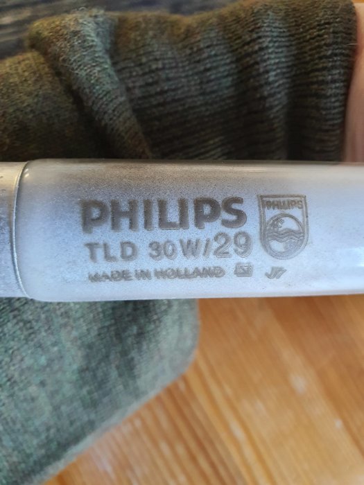 Hand som håller en Philips lysrörs lampa med etiketten visande modell TLD 30W/29, tillverkad i Holland.