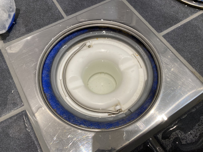 Närbild på en duschavlopp med överskott av fix och synlig klämring, inbyggd i ett kaklat golv.