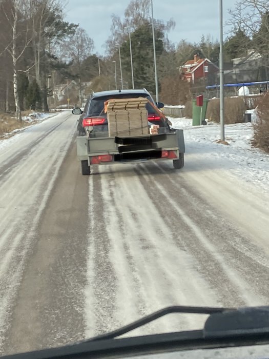 Bil med öppen baklucka transporterar osäkert fastsurrade träskivor på vinterväg.