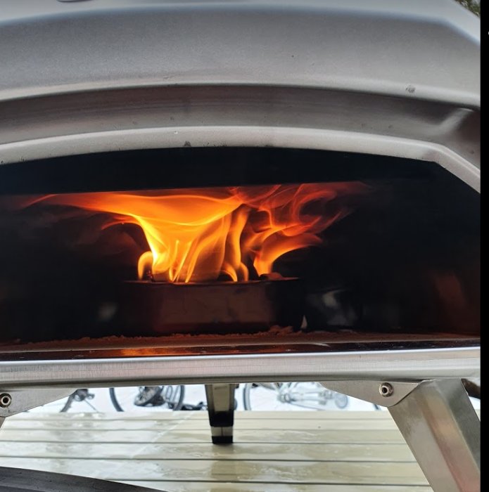 Lågor inuti en vedeldad ugn med synlig vedkorg, designad för omvandling till gasbrännare.