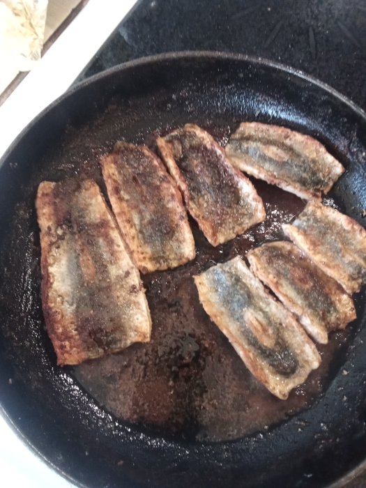 Stekt strömming i gjutjärnspanna, gyllenbrun och redo för servering med tillbehör.