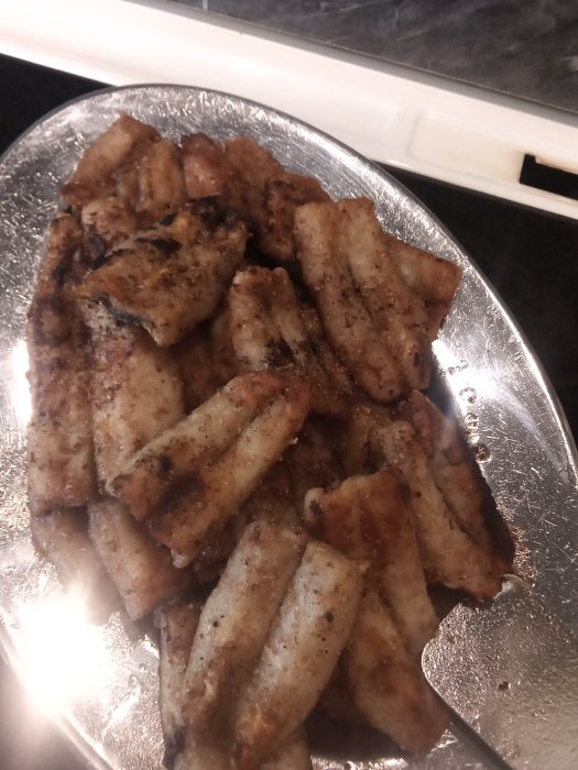 Stekt strömming på en tallrik, brun och krispig yta, redo för servering med tillbehör.