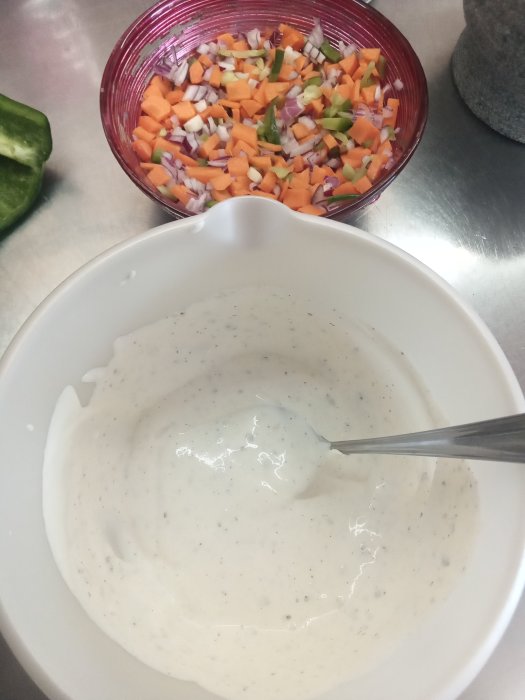 Hemgjord Rhode Island sås i vit skål och hackad rödlök, morötter, grön paprika i rosa skål.