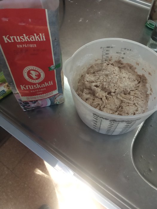 Bröddeg i en mätbägare bredvid en öppnad påse av Kruskakli på ett köksbord.