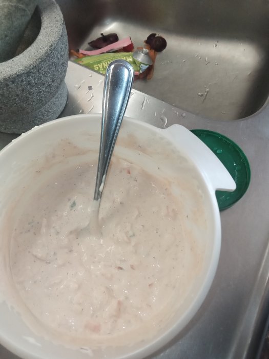 Hemgjord Rhode Island-sås i en vit skål med sked, hackad rödlök och paprika syns i blandningen.