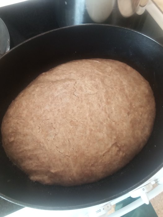 Ett hemgjort bröd i en gjutjärnsgryta redo att penslas med olja och saltas.