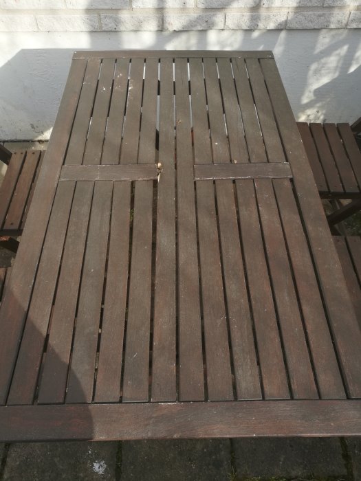 Brunbetsat träbord med lösa ribbor på en utplats, redo för renovering och ommålning.