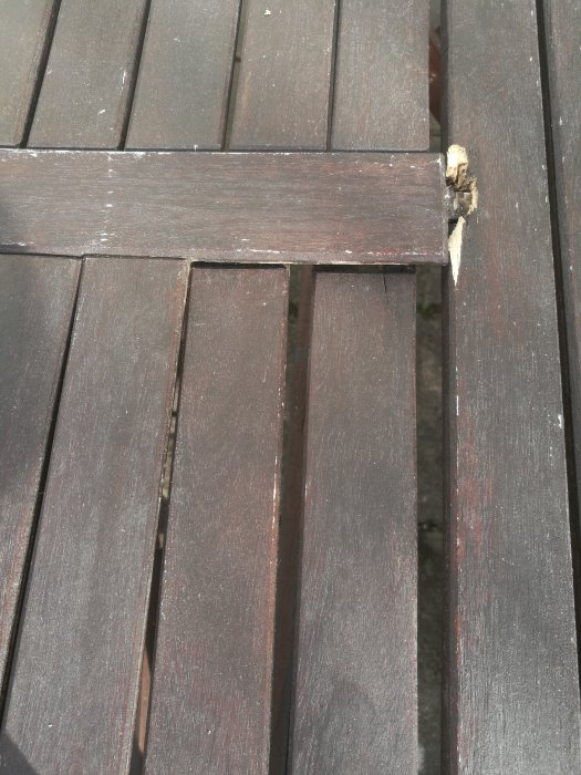 Brunbetsat träbord med lösa bordsskivor och synlig skada på en ribba.