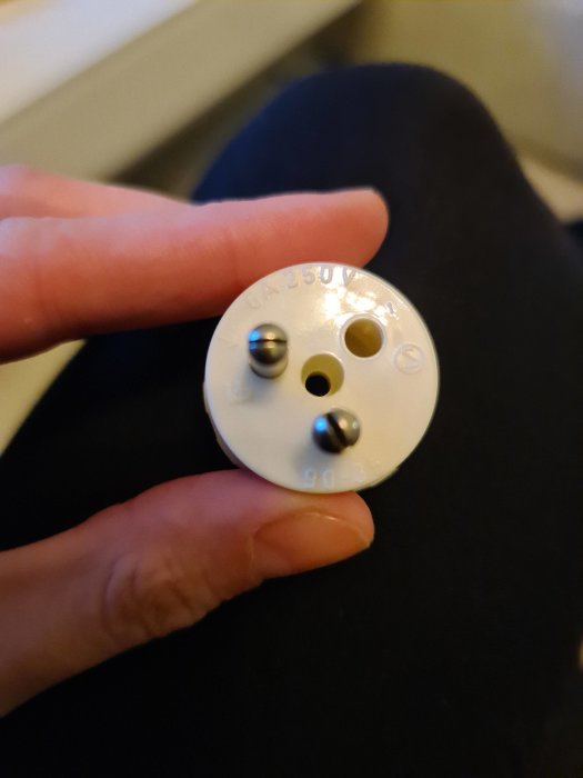En hand håller en vit ojordad lamppropp med två anslutningsterminaler.