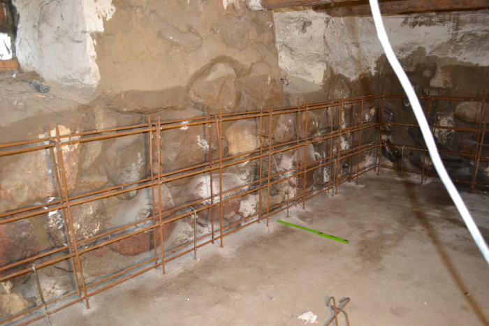 Renoveringsarbete med armeringsjärn framför en gammal stenmur och betongplatta.
