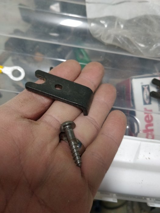 Hand håller en svart metallspak och en skruv mot en bakgrund av verktygsdelar.