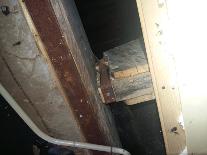 Synligt trä- och takbjälklag med konstruktionsmaterial och isolering som skymtar i bakgrunden i ett hus på vinden.