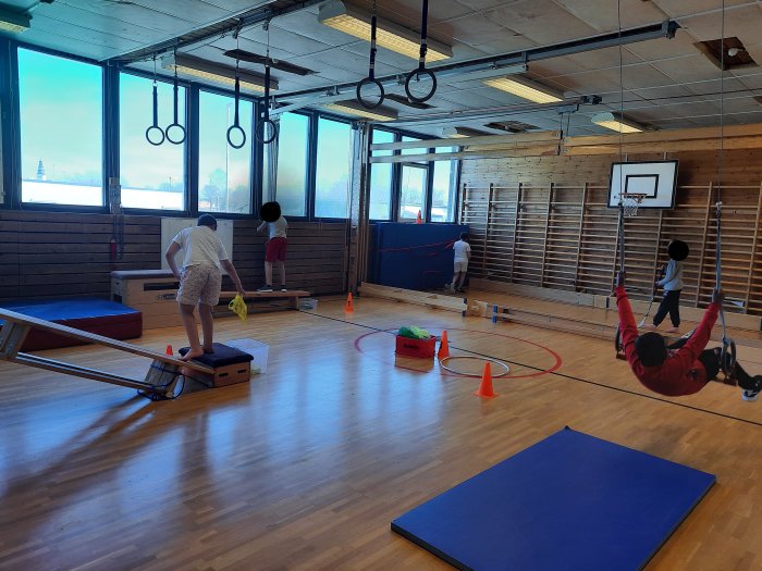 Barn leker och tränar i en gymnastiksal med bland annat ringar och en basketkorg.