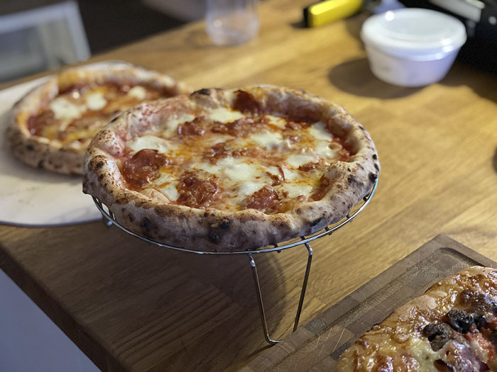 Hemmagjord pizza med bubblande ost och tomat på en stål ugnsställning, ytterligare en pizza i bakgrunden.