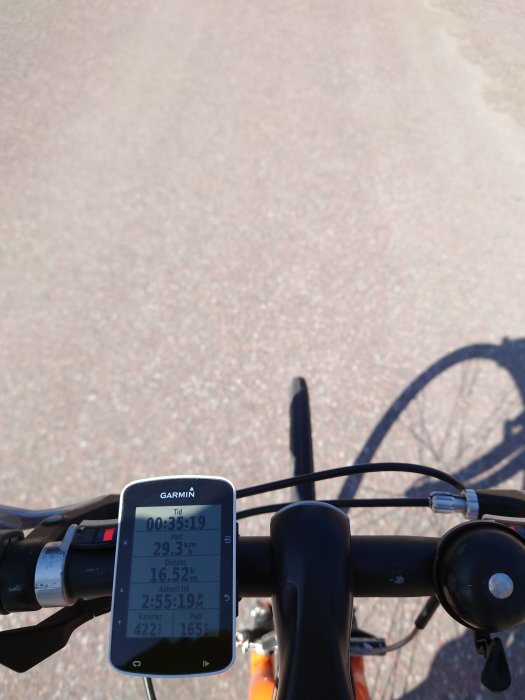 Cyklistperspektiv med cykeldator visar hastighet och distans, skugga av cyklist på vägen.