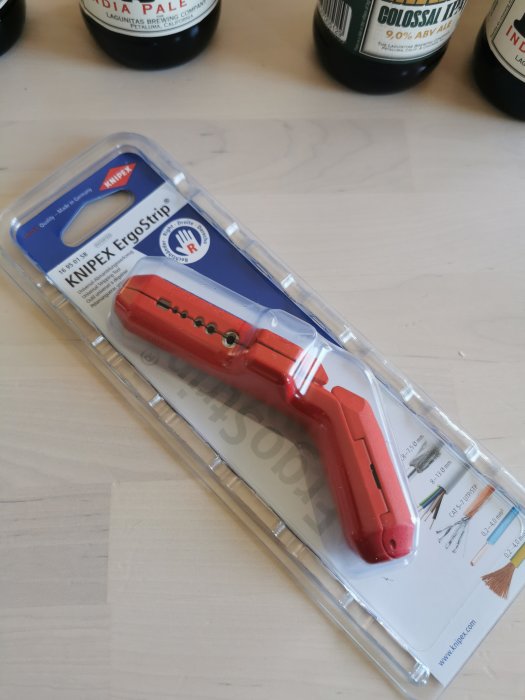 Nya Knipex ErgoStrip universal avmantlingstång i förpackning på ett bord med två ölflaskor i bakgrunden.