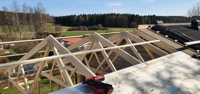 Nybyggda takstolar på ett hus med landskap i bakgrunden och en spikpistol i förgrunden.