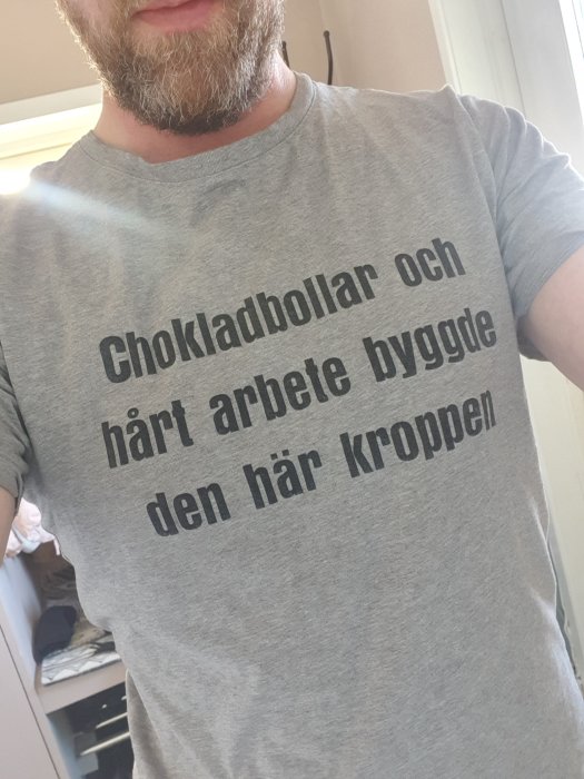 Person i grå tröja med texten "Chokladbollar och hårt arbete byggde den här kroppen