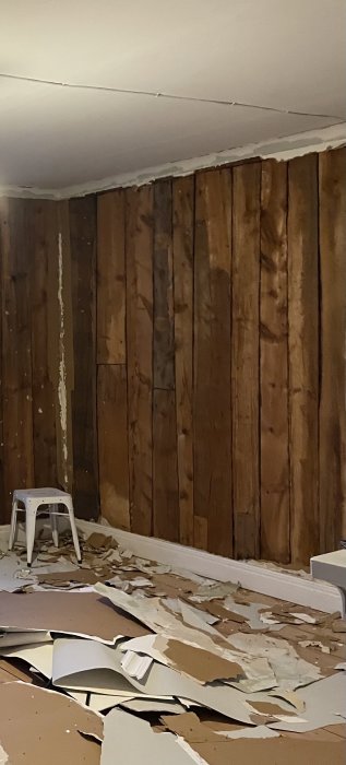 Renoveringsarbete med synliga stående träplank på vägg och rivet väggmaterial på golvet.