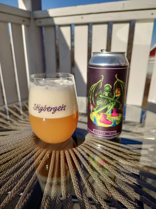 Ett glas öl och en burk med etikett av skelett på balkongbord, Dry & Bitter TIPA.