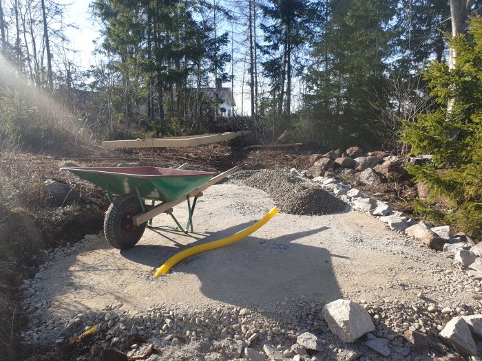 Grusområde med form för gjutning, skottkärra och omgivande natur, i förberedelse för armering och avvägning.