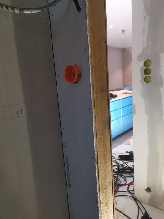 Utrymme med öppen vägg där en ny röd lysknapp är installerad, synliga kablar och en del av en dörröppning.