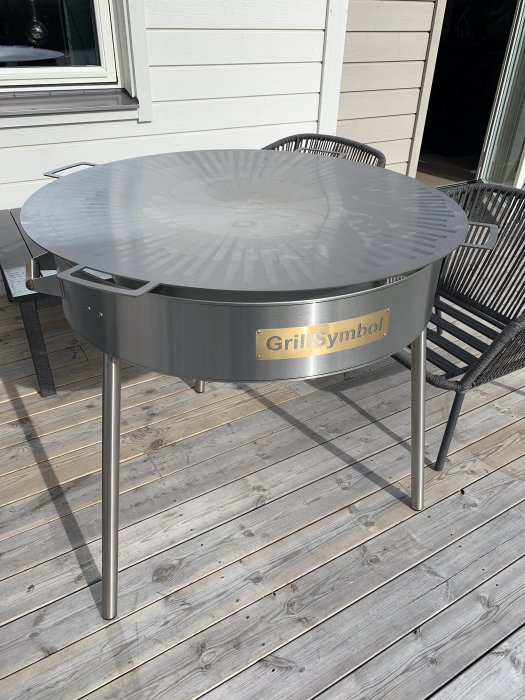 Rund stekhäll från GrillSymbol på en träaltan, bredvid trädgårdsstolar.