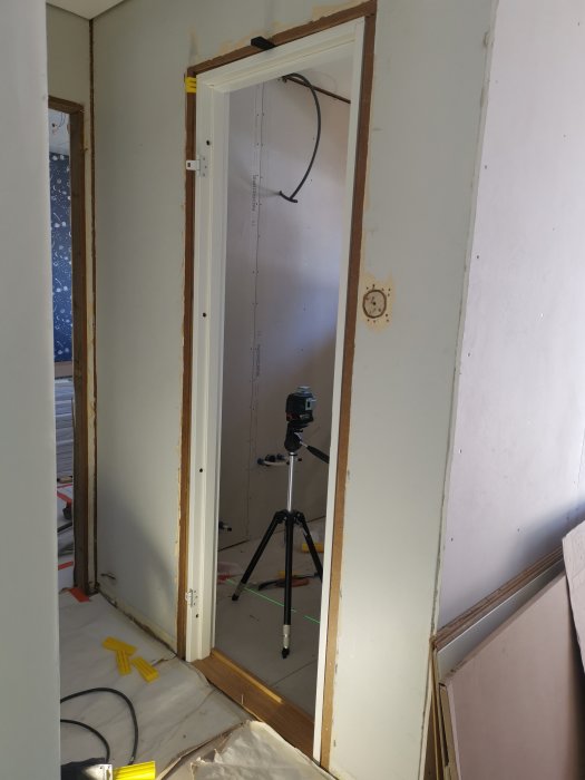 Nyinstallerad dörrkarm i ett renoveringsprojekt med synliga karmskruvar och ett laserpass i bakgrunden.