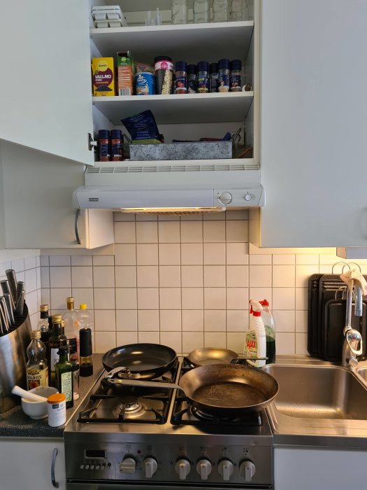 Kök med en vit köksfläkt ovanför en rostfri spis, utan synlig ventilationsanslutning.