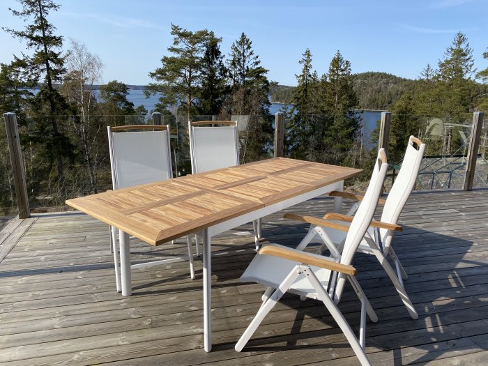 Uteserveringsgrupp med bord och stolar på trädäck med utsikt över skog och sjö.