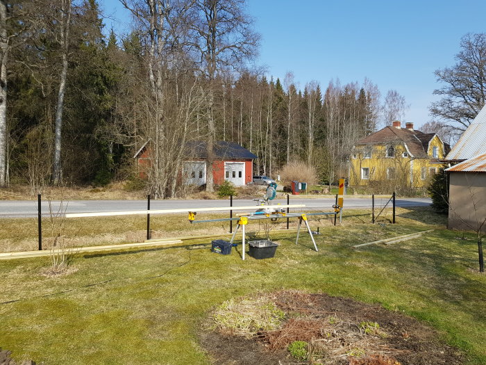 Uppställning av nya stolpar och reglar för staketbygge på en ojämn tomt med verktyg och material synligt.
