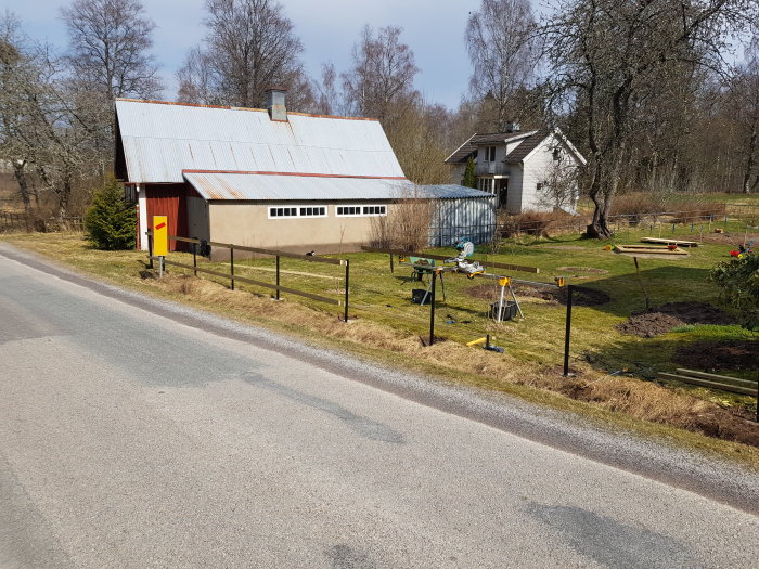 Stolpar med borrade hål och påbörjade reglar på en lutande tomt med lantlig miljö.