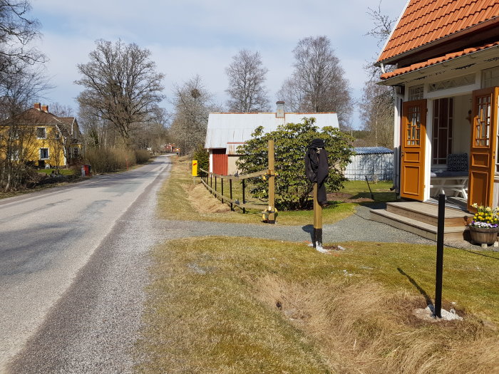 Nyuppförda trästolpar med borrade hål för reglar längs en lutande tomt vid en landsväg, nära ett traditionellt hus.
