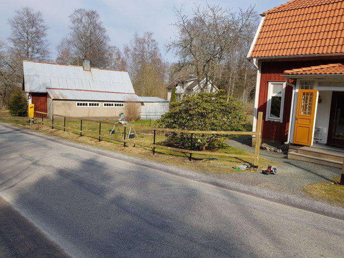 Trästaket under konstruktion med reglar på stolpar framför ett svenskt hus, verktyg på marken.