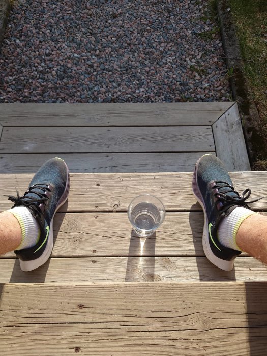 Person sitter på en trätrall med sneakers och en genomskinlig plastmugg framför sig.