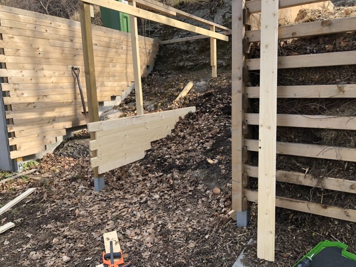 Uppbyggnad av ett nytt träkompostfack intill ett befintligt fyllt kompostfack i en trädgård.