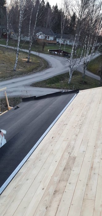 Nyinstallerad takpapp på halva taket av ett hus i skymningen, med träreglar som väntar på att bli täckta.