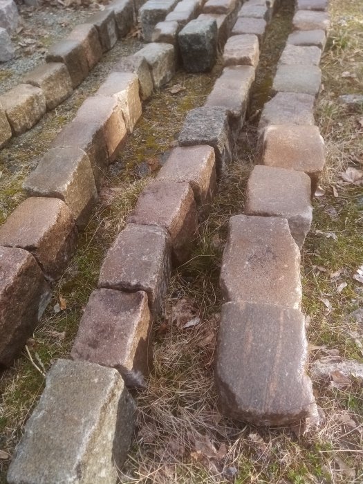 Två rader med gamla handhuggna storgatstenar anlagda på gräsmark.